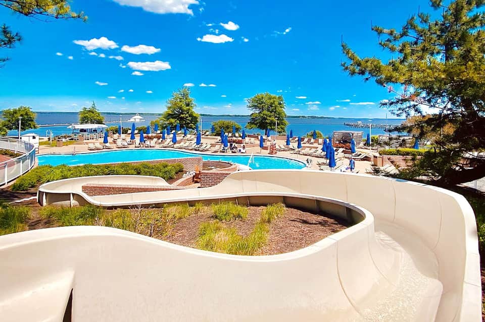 Waterfront pool complex with water slides, blue umbrellas, and scenic lake view