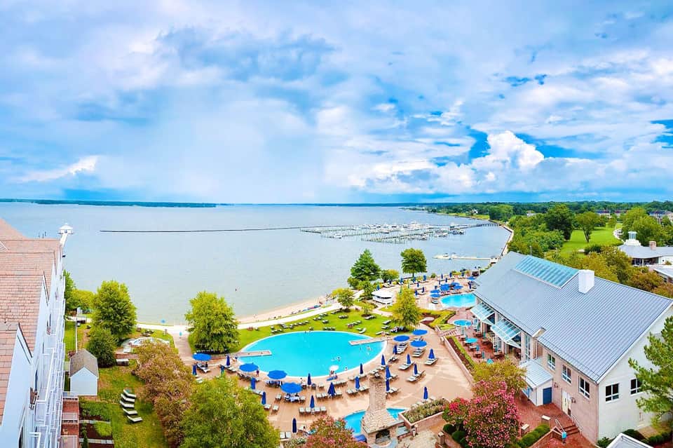 Aerial view of beachfront resort with pools, umbrellas, and bay waterfront