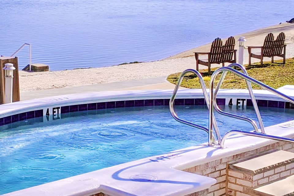 Outdoor swimming pool with metal ladder and Adirondack chairs on sandy beach overlooking calm blue water