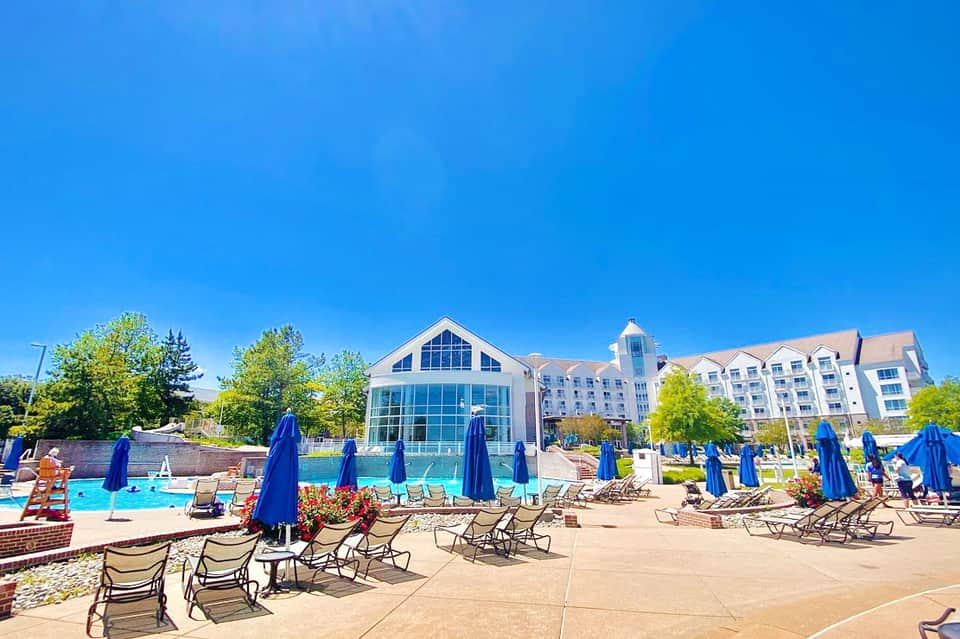 Resort pool area with blue umbrellas, lounge chairs, and modern hotel building in background