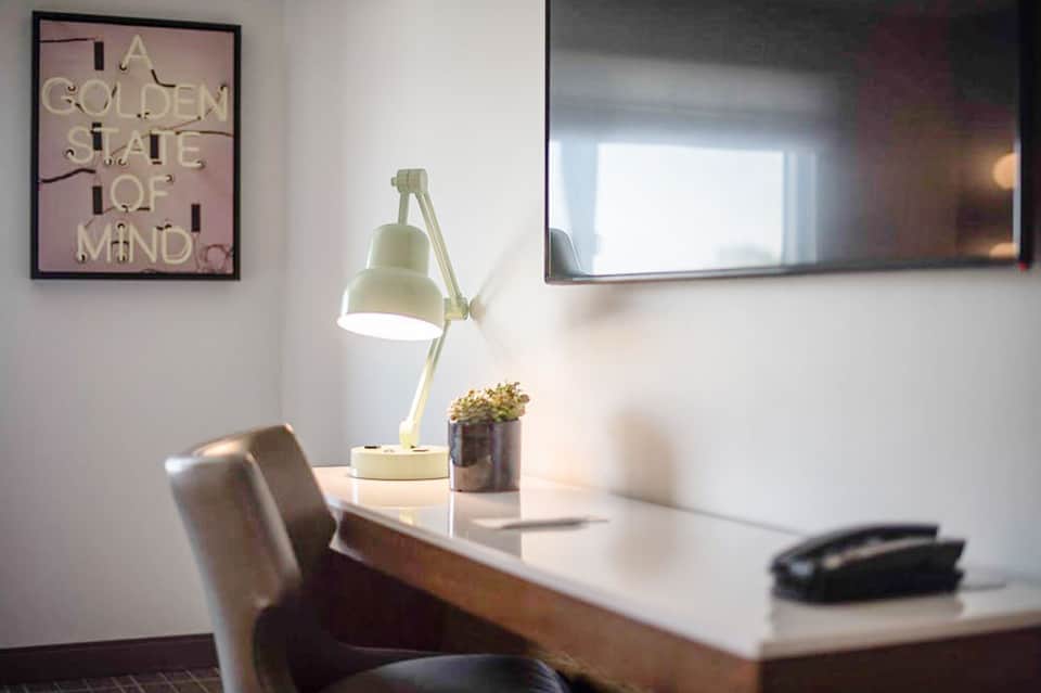 Minimalist office workspace with pale yellow desk lamp, potted plant, and neon pink wall art
