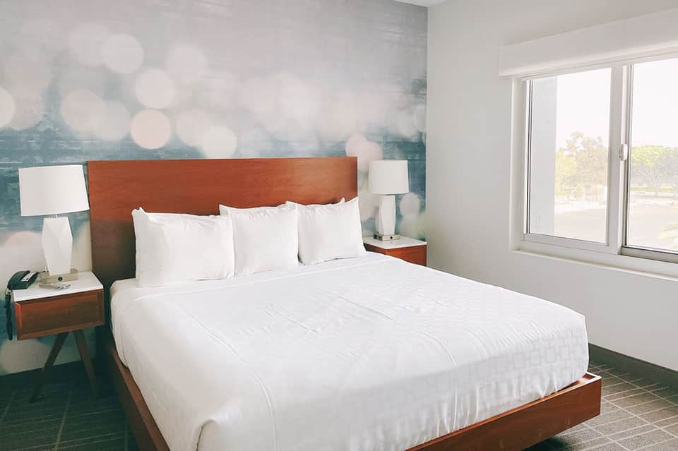 Hotel bedroom with wood headboard, white bedding, side tables with lamps, and view through glass doors