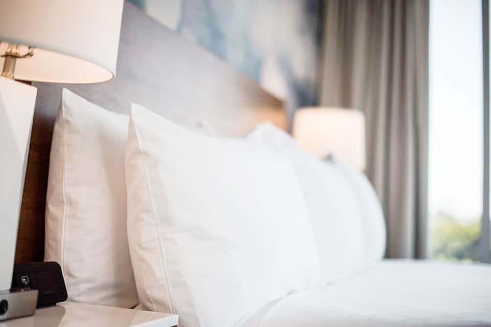 Luxury hotel bedroom with white pillows, bedside lamp, and curtains with ocean view