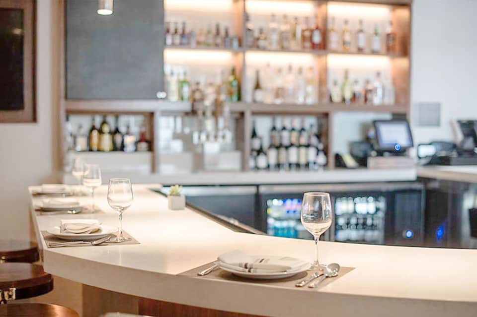 Modern fine dining restaurant with white counter seating and full bar in background