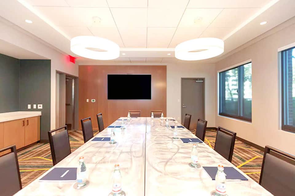 Professional conference room with long marble table, black chairs, TV screen, and modern ceiling lights.