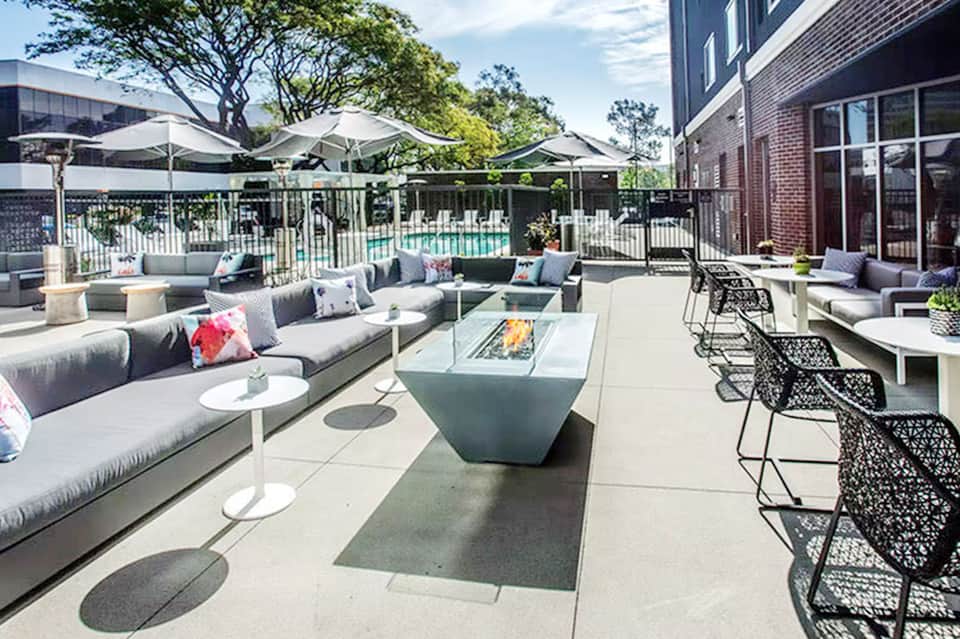 Modern outdoor terrace with gray sectional seating, fire pit, and metal chairs surrounded by landscaping