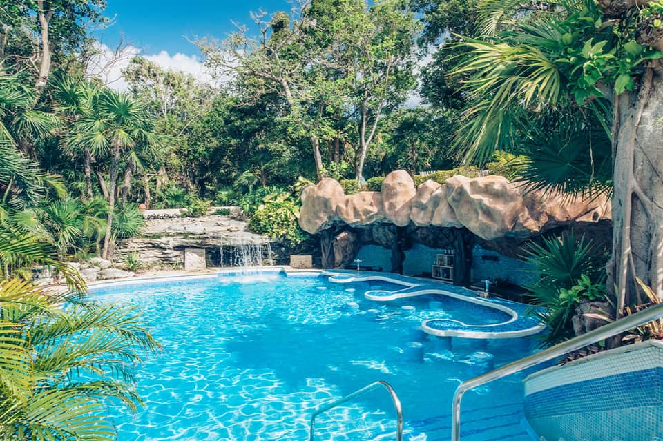 Blue swimming pool surrounded by lush tropical vegetation and stone waterfall feature