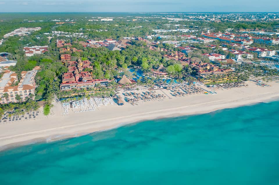 Aerial view of beachfront all-inclusive resort with red-roofed buildings, beach umbrellas, and turquoise Caribbean waters
