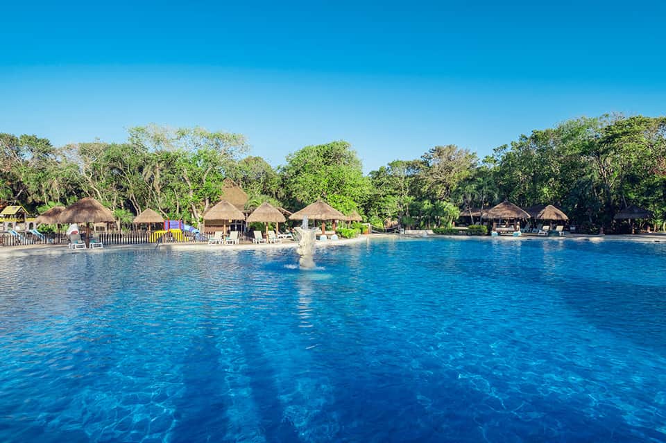 Tropical beachfront resort with thatched-roof buildings and clear blue water