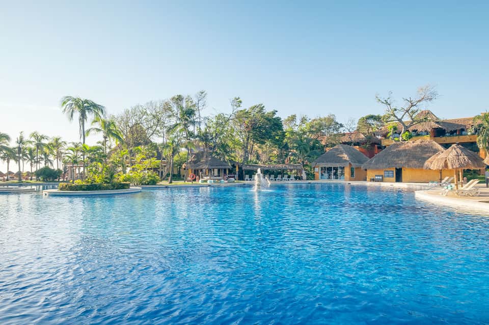 Resort pool with tropical landscaping, fountain, and thatched-roof structures