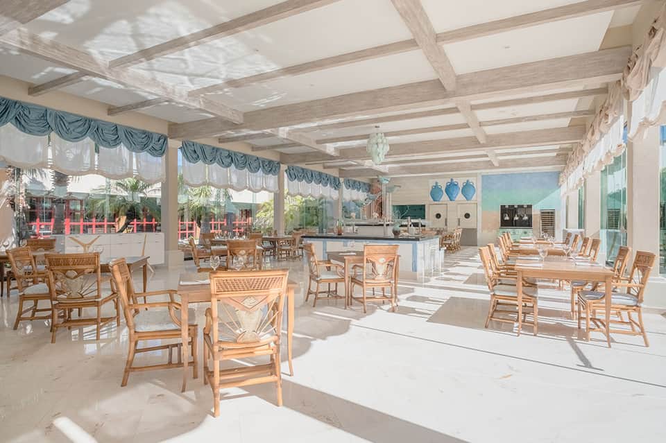 Bright dining area with wooden beamed ceiling, skylights, rattan chairs, and ocean views through glass doors