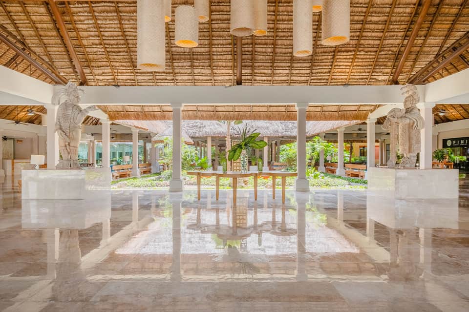 Modern spa lobby with polished marble floors, white columns, thatched ceiling details, and decorative statues