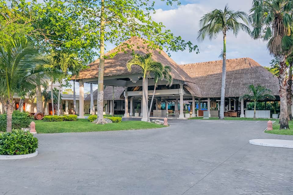 Contemporary thatched-roof pavilion with supporting columns and manicured lawn surrounded by palm trees