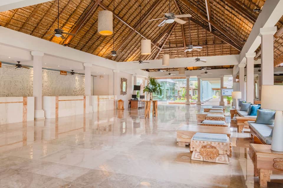 Spacious resort lobby with high thatched ceiling, marble floors, and tropical plants