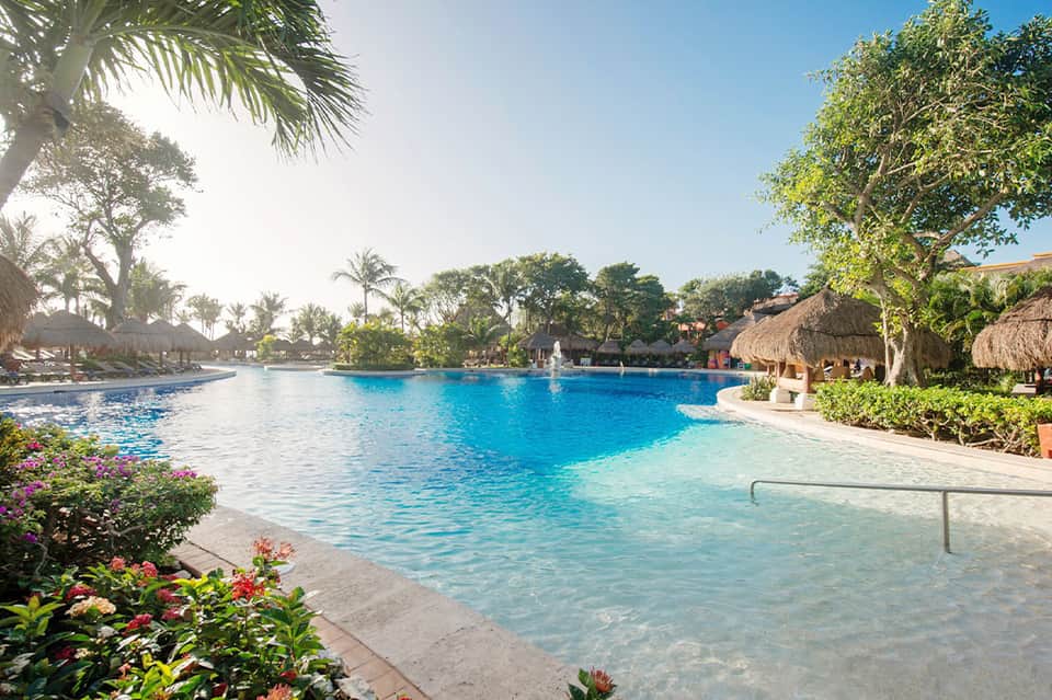 Resort lagoon pool with thatched-roof cabanas, palm trees, and tropical landscaping at dusk