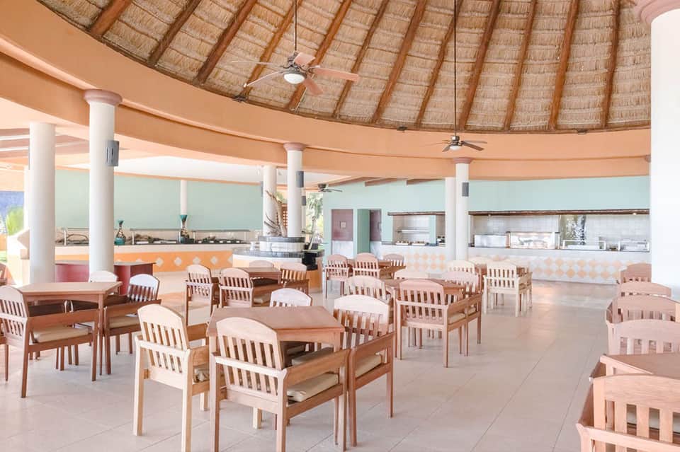 Beige and white dining area under thatched roof with round tables and wooden chairs
