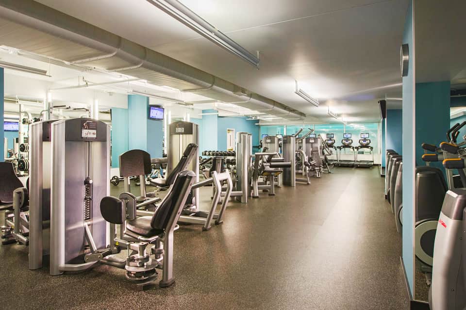 Modern gym with turquoise walls, extensive exercise machines, and bright fluorescent lighting