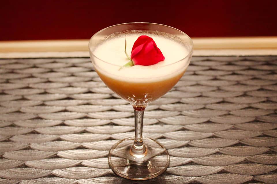 Elegant cocktail with layered brown and cream liqueur, topped with a red rose petal and green leaf