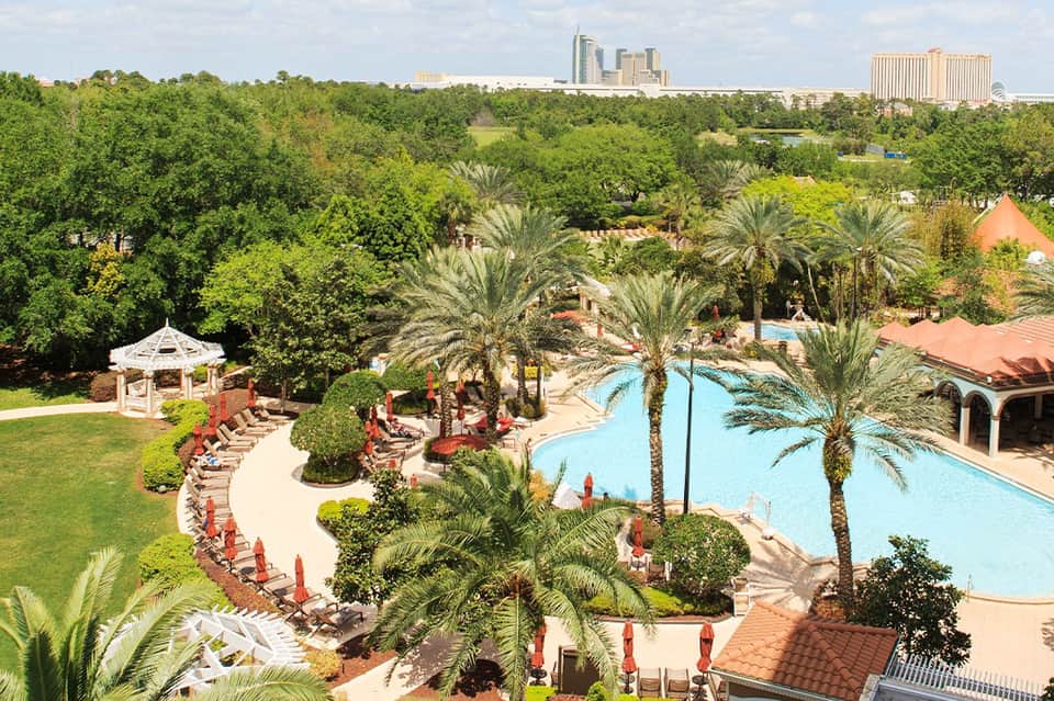 Aerial view of resort pool complex with palm trees, loungers, and downtown city skyline in background
