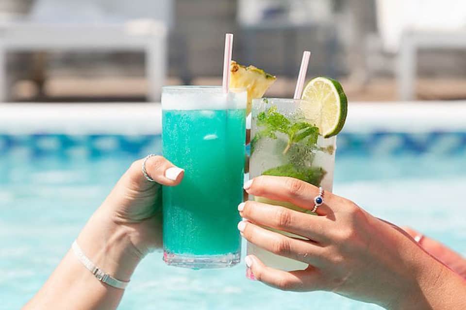 Two colorful cocktails by the pool - turquoise and lime green drinks with garnishes and straws