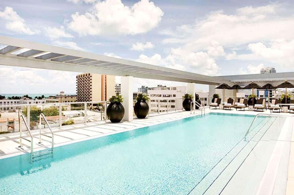 Modern rooftop swimming pool with turquoise water, lounge chairs, umbrellas, and city skyline views
