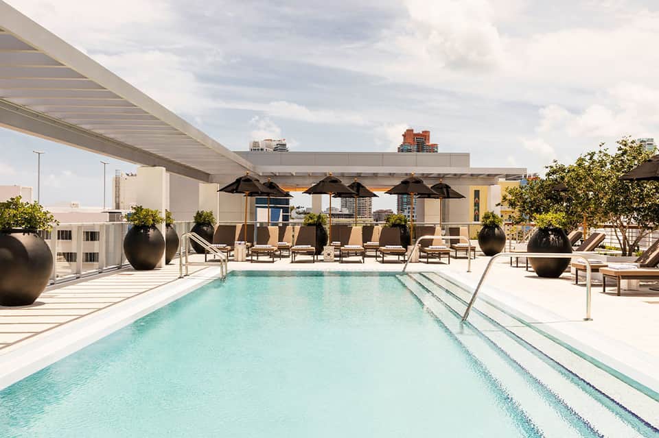 Rooftop lap pool with lounge chairs and umbrellas overlooking urban cityscape