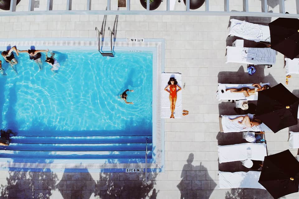 Aerial view of hotel pool with swimmers and guests lounging on deck chairs