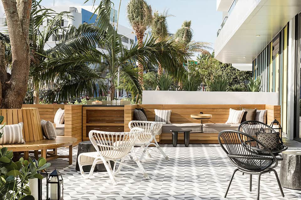 Outdoor terrace with wooden bench seating, woven chairs, and tropical plants surrounding patio space