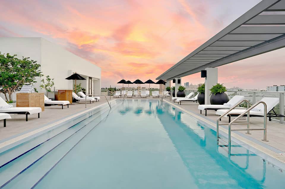 Lap pool at sunset with black umbrellas, loungers, and dramatic pink and orange sky above