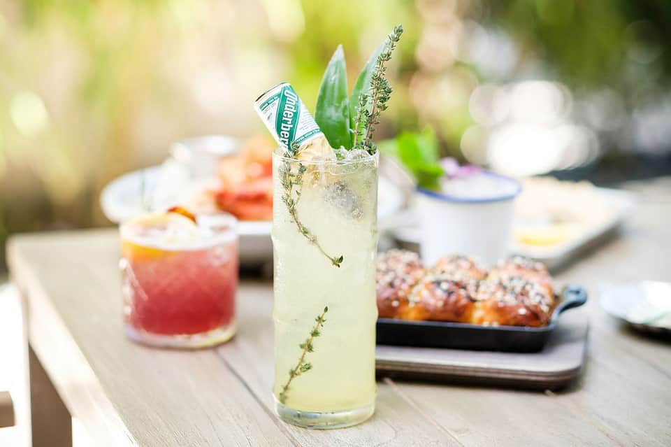 Refreshing cocktail with herbs garnish surrounded by appetizers on outdoor table