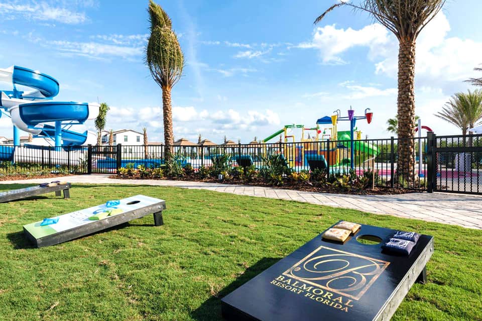 Outdoor lawn games and water slide at family resort with palm trees and colorful playground