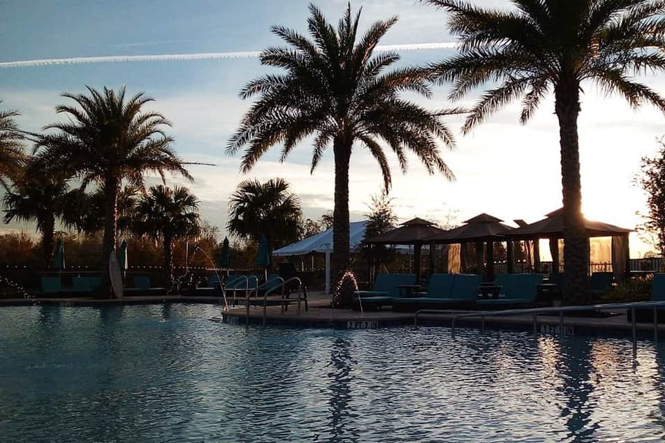 Waterfront sunset view with palm trees, covered pavilions, and lounge chairs by the water
