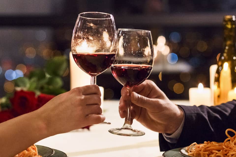 Two wine glasses clinking in a romantic dinner toast with candlelight