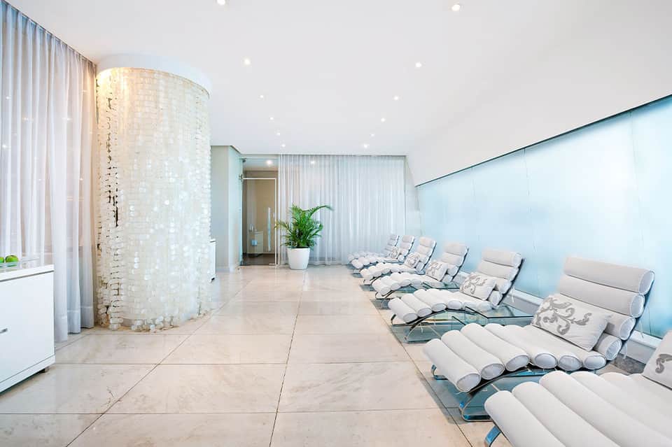 Modern spa relaxation room with light blue walls, white lounge chairs, and exposed brick column