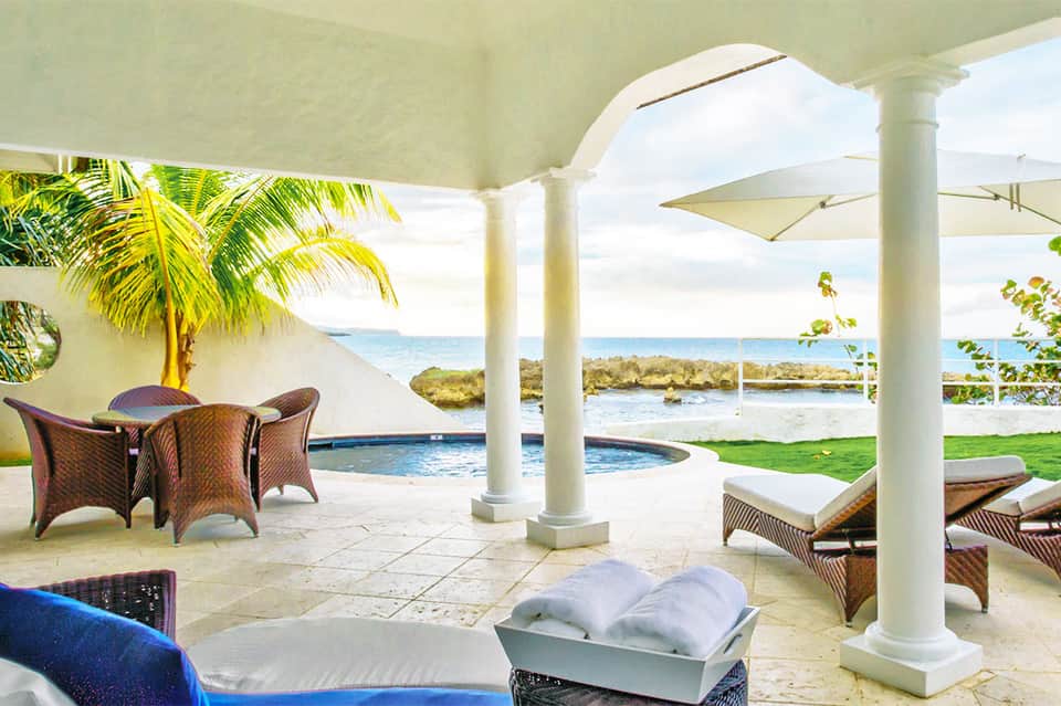 Beachfront terrace with lounge chairs, palm tree, pool, umbrellas, and ocean view