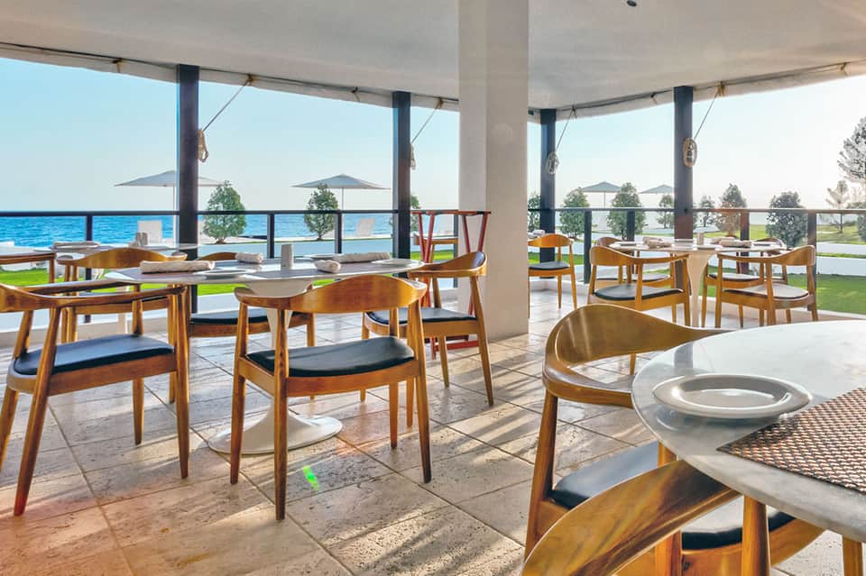 Waterfront dining area with wooden chairs and ocean views through large windows