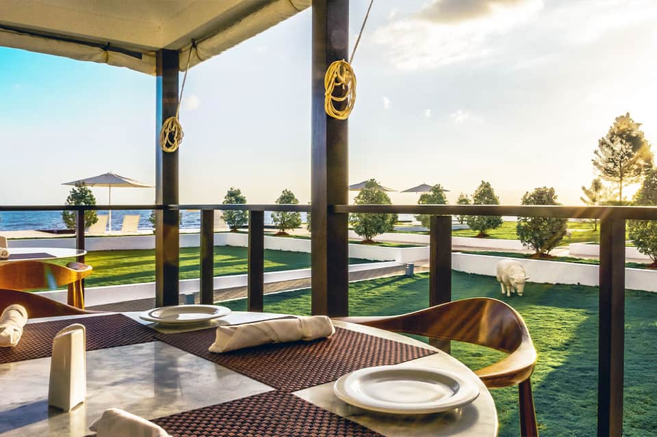 Waterfront dining setup with table settings, ocean view, and manicured green lawn with decorative elements