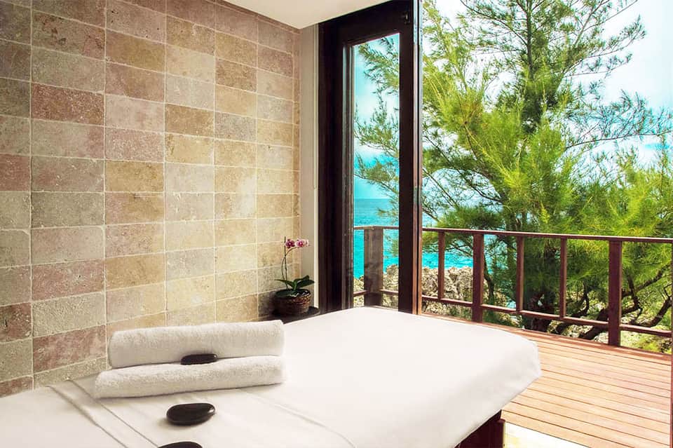 Spa massage room with ocean view through glass door and tropical plants