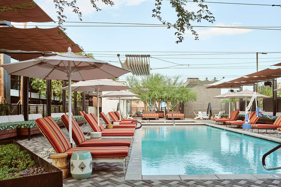 Resort pool with red striped lounge chairs, white umbrellas, and brick buildings in background