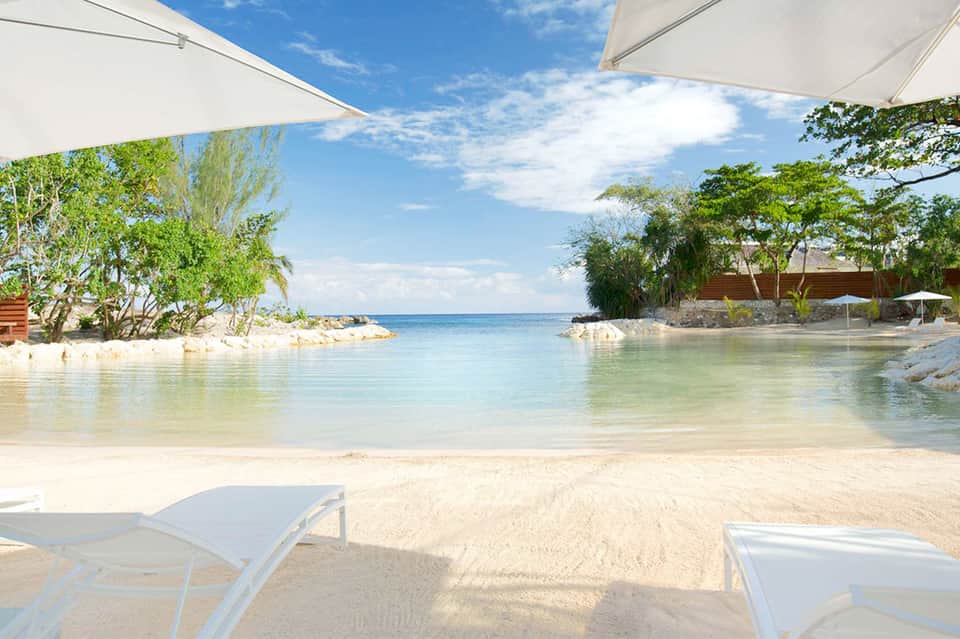 Pristine beach cove with white sand, turquoise water, and white umbrellas among tropical trees