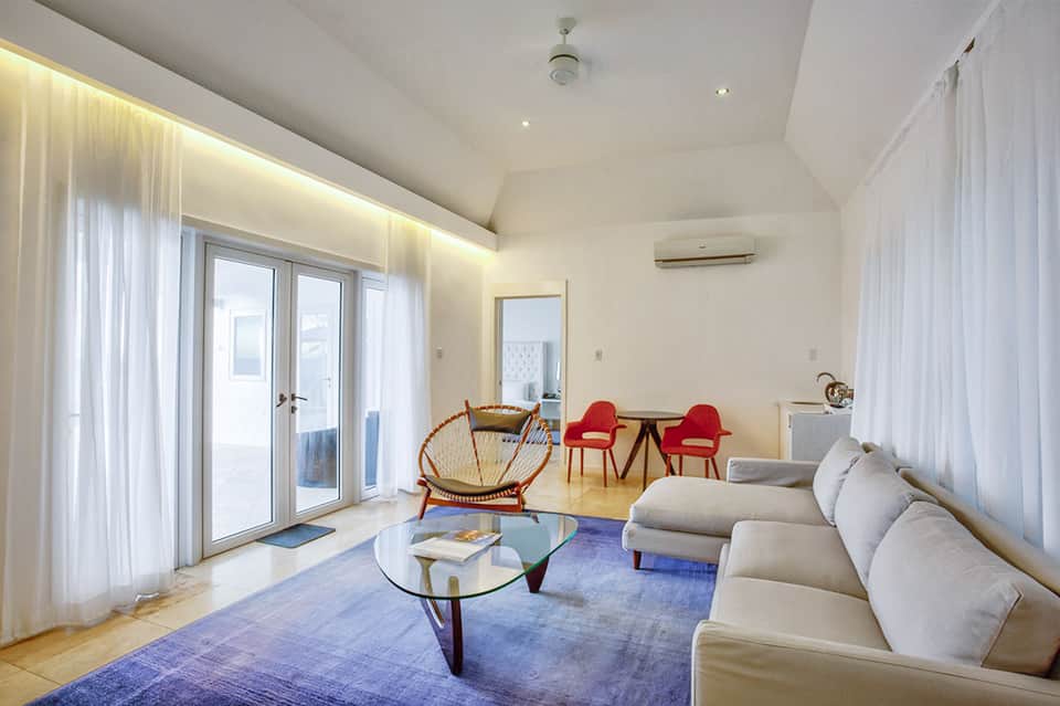 Modern resort suite with cream sofa, red accent chairs, glass coffee table, and ocean view balcony