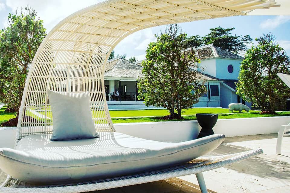 White curved woven lounge chair with cushion on terrace overlooking modern turquoise house and gardens
