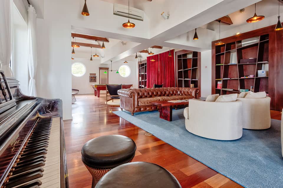 Modern lounge with piano, red leather furniture, white curved seating, and wooden shelving