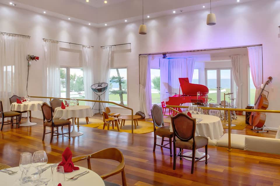 Elegant dining room with white tablecloths, red piano, ocean views, and sophisticated lighting