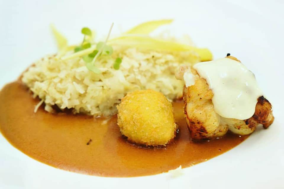 Plated seafood dish with scallops, crispy potatoes, sauce, and herb garnish on white background