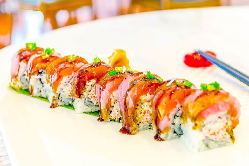 Artfully arranged sushi rolls on white plate with decorative orange and red toppings and green garnish