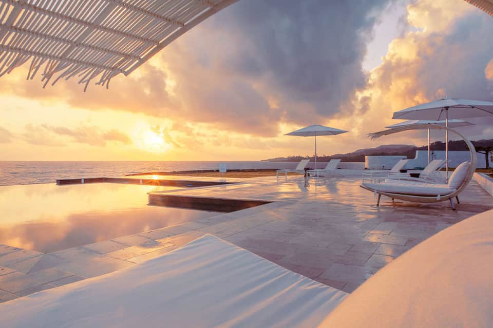 Sunset over infinity pool with white lounge chairs and ocean horizon at dusk
