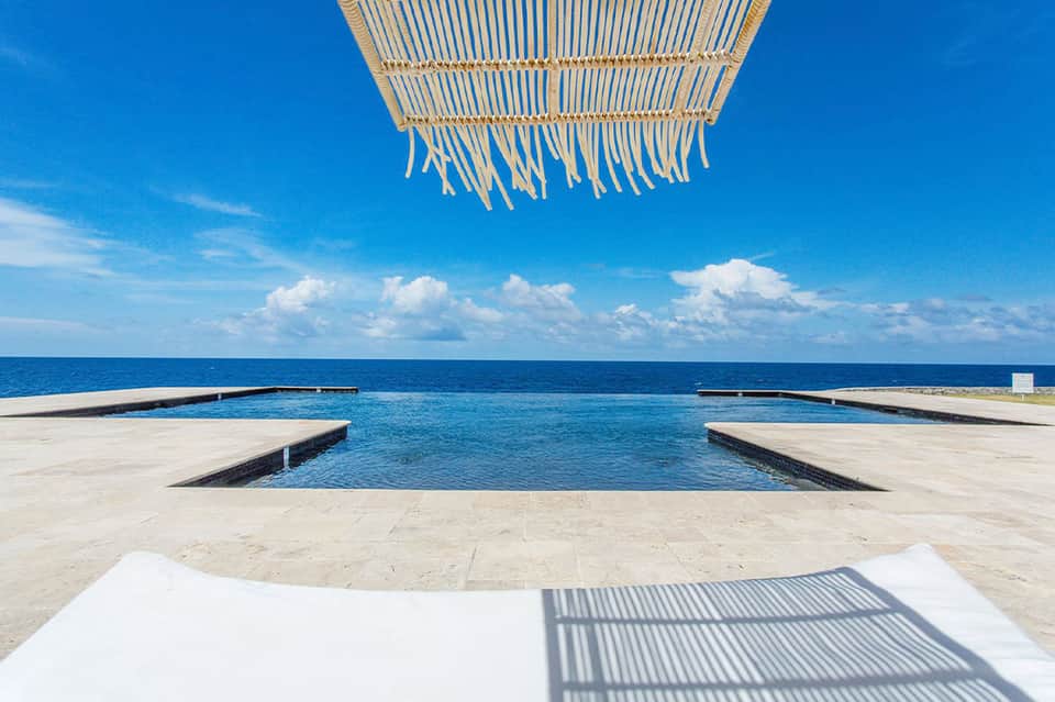 Oceanfront infinity pool with woven shade structure and turquoise water meeting horizon