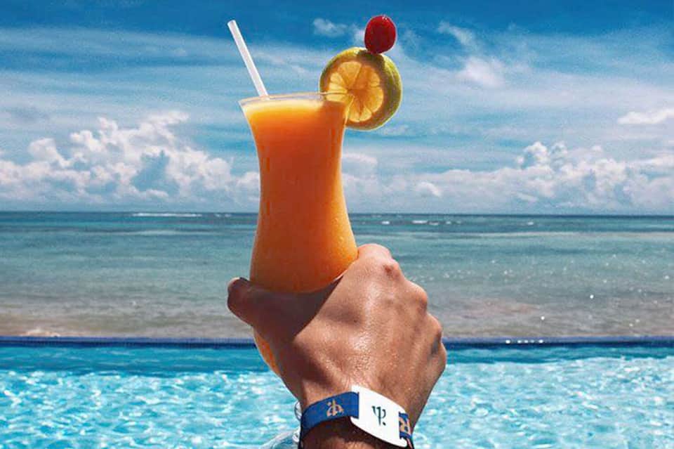 Hand holding tropical cocktail with orange slice and cherry over ocean view
