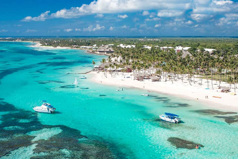 Aerial view of turquoise Caribbean waters, white sand beach, and palm trees with boats